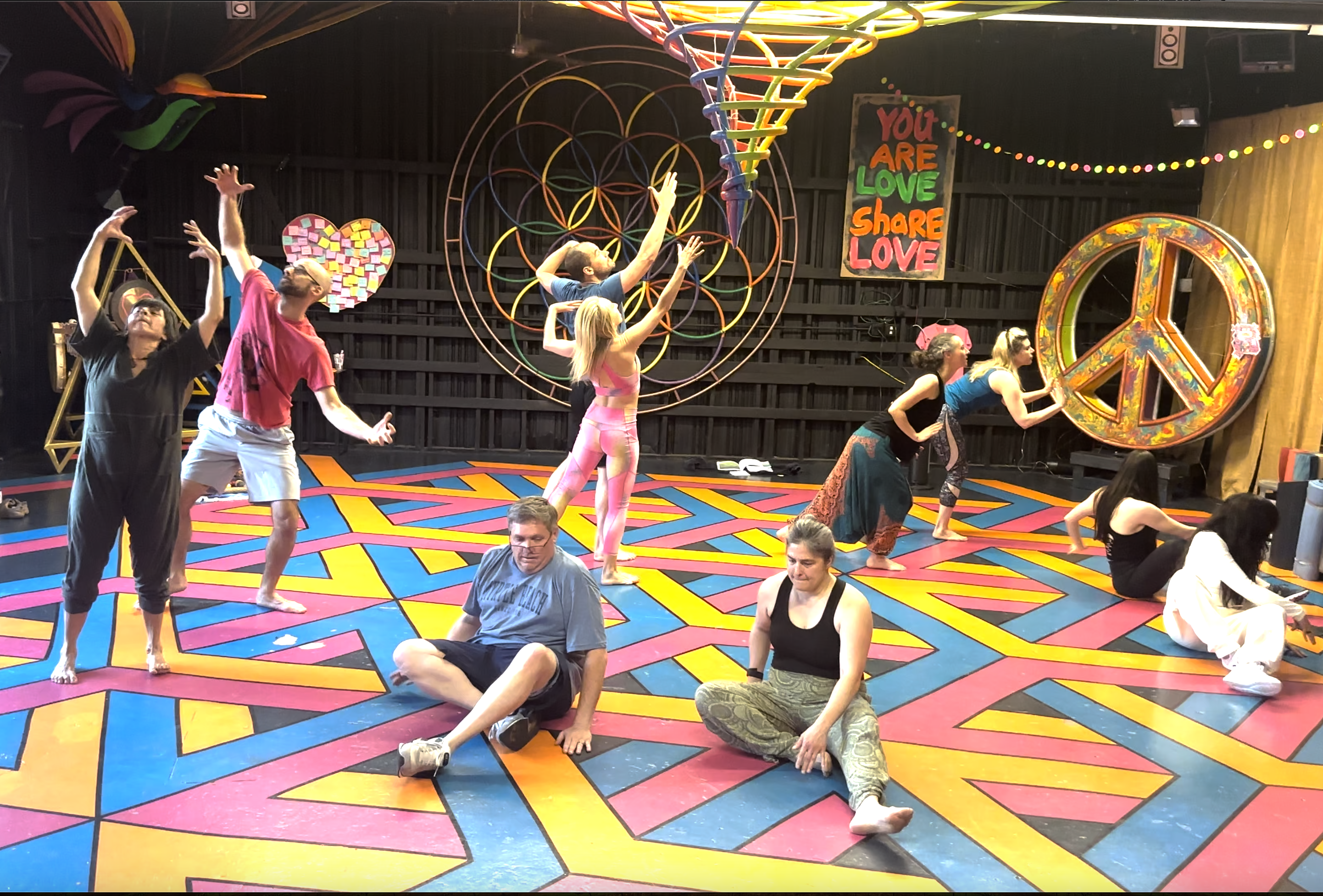 A group of dancers in a colorful room are performing a group dance made of multiple duets.